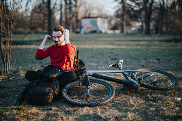 A young adult male relaxes in a park, adjusting his hair beside his mountain bike, enjoying a peaceful outdoor break.