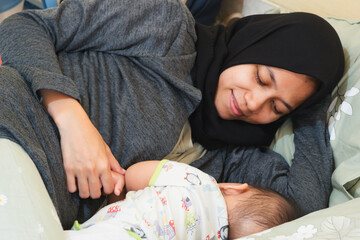 An Asian Muslim mother is looking at the face of her sleeping baby with great affection