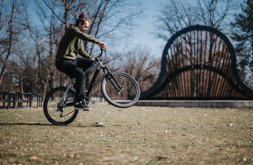 Fototapeta premium A young adult male cycles confidently in a vibrant park, showcasing dynamic motion and a scenic backdrop with an iconic bridge.