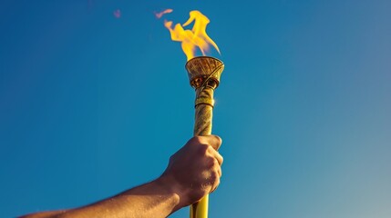 A man's hand holds a torch with the olympic flame against a blue sky background. Sport concept