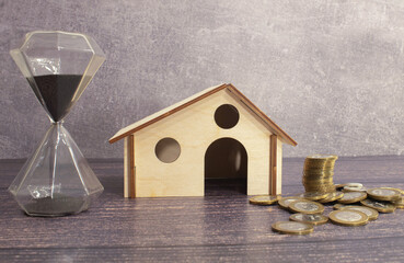 stack of coins with house model and hourglass on table