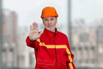 Mature construction worker handyman shows the no reject gesture sign. Blurred indoor windows background.