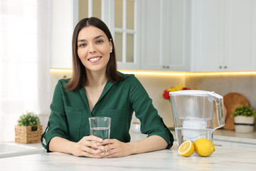 Woman with glass of water and filter jug in kitchen