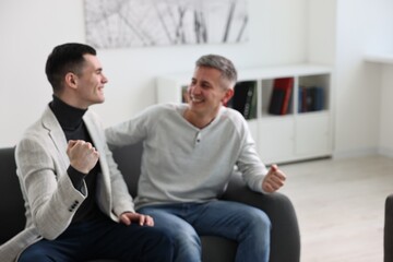 Blurred view of happy men talking while sitting on sofa at home