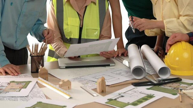 Smart architect and safety engineer discussion about building blueprint on table with architectural document, measurement tools and wooden block scatter around at modern office. Closeup. Delineation.