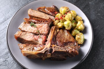 Delicious fried beef meat, vegetables and thyme on black table, closeup