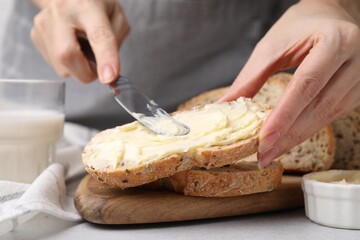 Woman spreading tasty butter onto bread at table, closeup