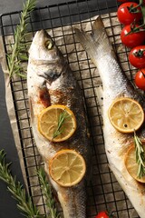 Baked fish with tomatoes, rosemary and lemon on black table, top view