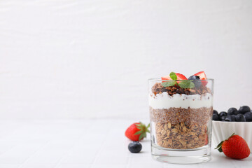 Tasty granola with berries, yogurt and chia seeds in glass on white tiled table, space for text