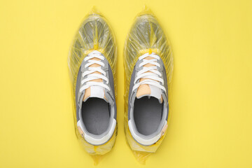 Sneakers in shoe covers on yellow background, top view
