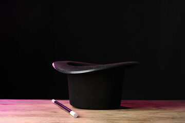 Magician's hat and wand on wooden table against black background