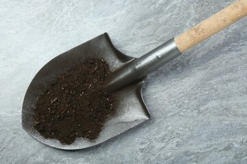 Metal shovel with fertile soil on gray textured surface, top view
