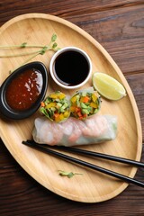 Tasty spring rolls and sauces on wooden table, top view