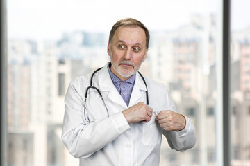 Portrait of a male doctor hiding money in his pocket. Blurred indoor background.