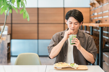 カフェでランチを食べながらグリーンスムージーを飲む若い男性（酵素・ヘルシー・食物繊維・健康食品）
