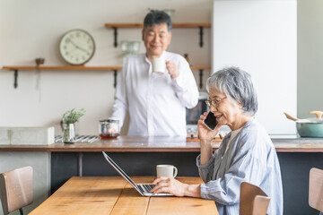 Obraz premium 家でパソコンを使う高齢者女性とキッチンにいる高齢者男性 