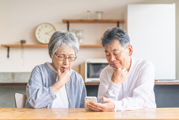 スマホ・スマートフォンのアプリを使うアジア人高齢者夫婦（困る・わからない・難しい・不安）

