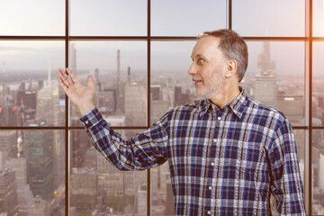 Handsome mature senior man presenting copy space with his hand. Checkered windows background with cityscape view.