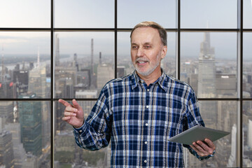 Happy cheerful aged man with tablet pc. Checkered windows background with cityscape view.