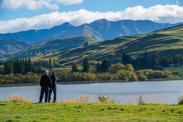 Father and son stand by the lake in the park admiring the lake mountain view in summer.

