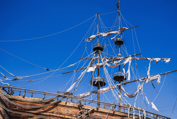 mast with sails on an ancient wooden pirate ship against a background of blue sky in ocean