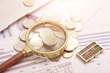 Coins, magnifying glasses, and abacus placed on data sheets - Monetary Finance