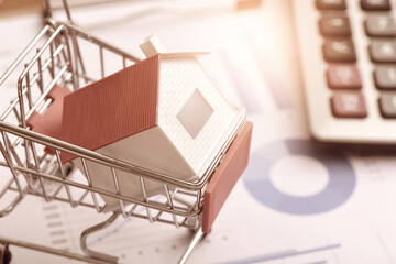 Calculator on data drawing report and small house model placed in shopping cart