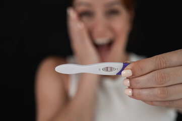 Blurred portrait of happy caucasian woman holding positive express pregnancy test on black...