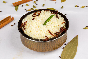 A traditional brass dish of Indian Pilau rice surrounded by spices such as bay leaf and cinnamon