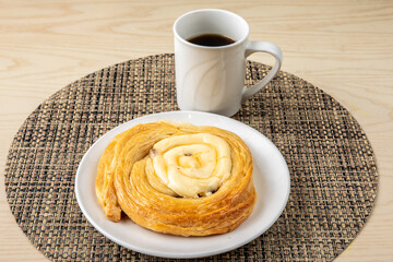 A cream cheese filled Danish pastry with a cup of coffee on a wooden table