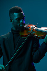 Elegant musician in black suit playing violin under blue spotlight on blue background, creating a serene atmosphere