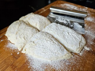 Raw bread dough lying on a wooden cutting board that has been cut into four quadrants by a metal bench scraper.