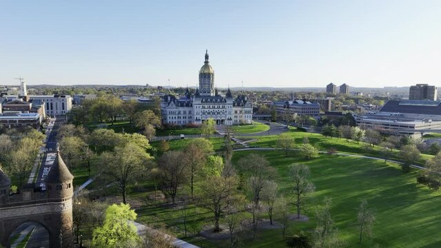 Wide establishing drone shot of the Connecticut State Capitol building on a sunny spring day with aerial view over Bushnell Park in Hartford, CT