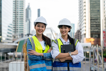 Two Asian female engineers looking at camera and standing arms crossed with a cityscape in the background