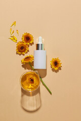 Unlabeled glass serum bottle arranged with a beaker of Calendula flower oil over beige background....