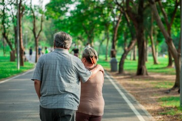 Obraz premium A man and woman are walking together on a path in a park. The man is wearing a gray shirt and the woman is wearing a pink shirt. They are holding hands and seem to be enjoying each other's company