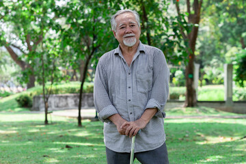 An older man is standing in a park with a cane. He is smiling and he is enjoying his time outdoors