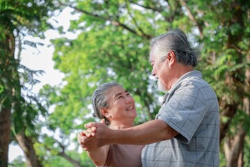A man and woman are dancing in a park. The man is wearing a gray shirt and the woman is wearing a brown shirt. They are both smiling and enjoying themselves