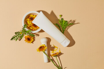 A mortar containing yellow flowers arranged with some green leaves and a beauty tube without label....