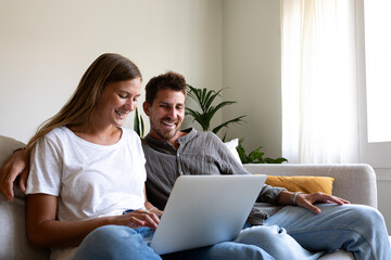 Happy young couple using laptop relaxing sitting on the sofa ordering online. Copy space.