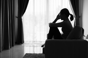 Depressed woman, Silhouette of teenager girl with depression sitting alone  in the dark room. Black and white photo.