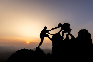 Silhouette of person hikers climbing up mountain cliff and one of them giving helping hand. People helping and, team work concept.