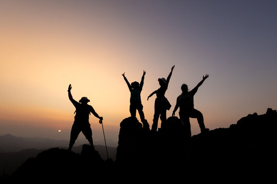 Silhouette of person hikers climbing up mountain cliff and one of them giving helping hand. People success, team work concept.