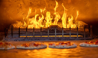 Wood fire pizza oven with selective focus on  flames and cement texture.  Four pizzas are in front...