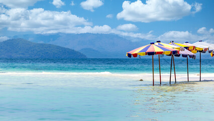 Umbrellas beach in the blue sea on sunny day, Beach umbrella on sandy coast in sea. - obrazy, fototapety, plakaty