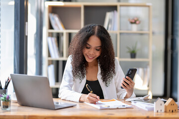 Cheerful professional woman waving to the smartphone during a friendly video call in a sunny office setting.