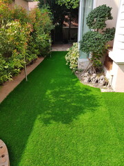 A backyard with green artificial grass fills most of the frame. The grass is smooth and uniform,...