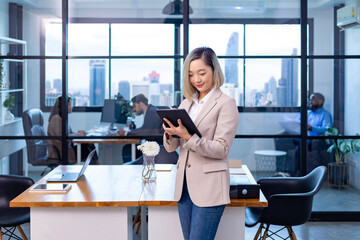 Portrait of Asian business CEO woman is standing in office at the table with digital tablet and...