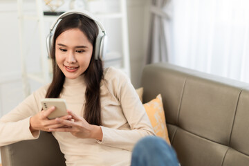 A brunette young asian woman relaxes on a couch sofa, lost in music with headphones  at home.