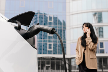 A businesswoman is waiting to charge her electric car in the parking lot of a business center with...